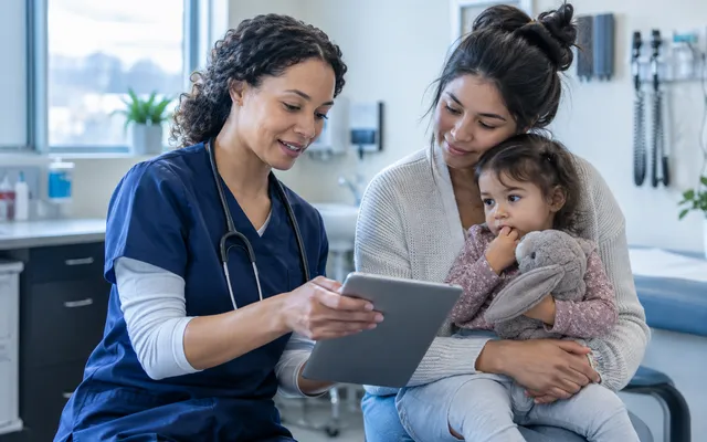 A nurse practitioner showing a tablet to a mother holding her toddler